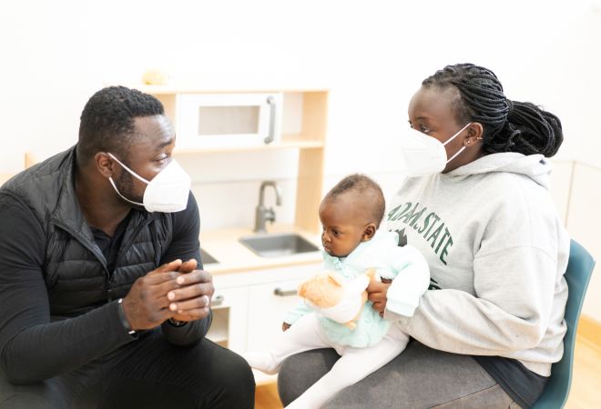 Baby Gabriella aus Uganda sitzt auf dem Schoß ihrer Mutter, die sich mit Gerald Asamoah unterhält.